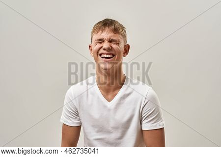 Excited Laughing Caucasian Teenage Boy With Closed Eyes. Blonde Guy Of Zoomer Generation Wearing T-s