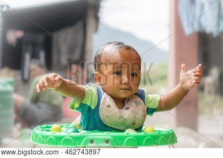 Kathmandu, Nepal - September 18, 2022: A Baby Asian Boy In A Walker Holding Out His Arms.