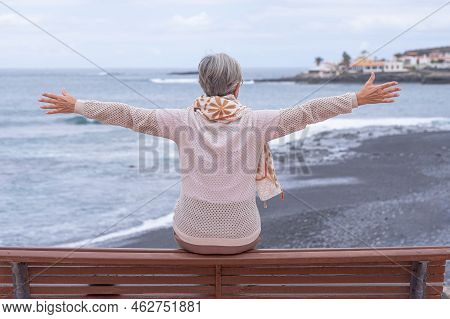Rear View Of Senior Woman Sitting On A Bench Face To The Sea Looking At Horizon Over Water. Active C