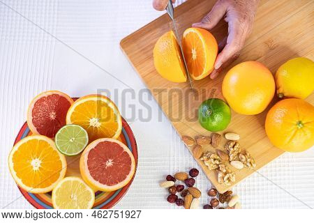 Group Of Whole And Halved Citrus Fruits, Wooden Cutting Board With Female Hand Cutting An Orange. Gr
