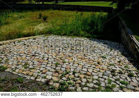 Restoration Of A Pond With A Stone Wall Buried Under The Terrain. Fire Tank With Beveled Stone Paved
