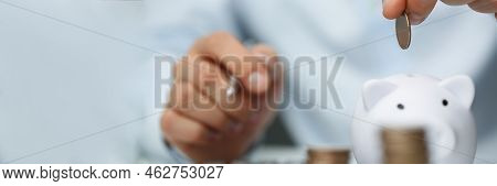 Close-up Of Person Accountant Put Coin In White Piggy Bank, Stack Of Coins On Workplace. Prepare Ann