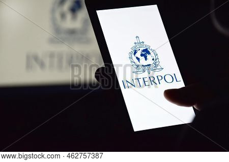 Person Holding Smartphone With Interpol Logo Displayed On Screen.