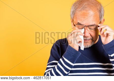 Asian Elder Man Crying Raise Glasses With Tissue Wipe Red Eyes Studio Shot Isolated On Yellow Backgr