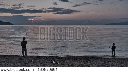 Maksimikha, Russia - August 13, 2022: Silhouettes Of Man And Boy Fishing With Fishing Rod On Sandy S