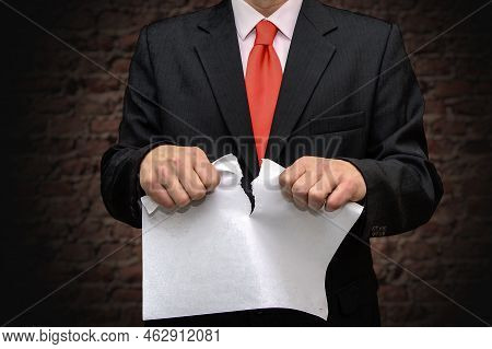 A Man In A Suit Tears Up A Piece Of Paper Against A Brick Wall. Concept: Termination Of The Contract