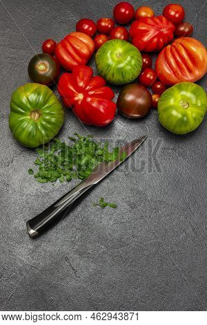 Different Varieties Of Red And Green Tomatoes. Chopped Parsley And Knife. Copy Space. Flat Lay. Blac