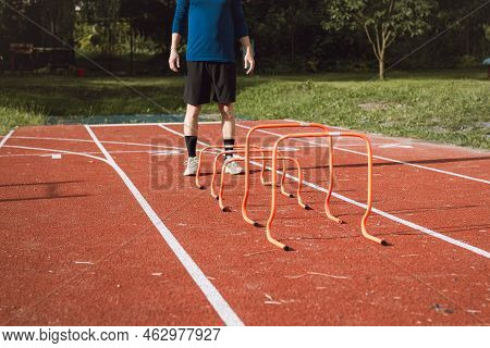 Blond Boy In Sportswear Jumps Over Red Obstacles To Improve Lower Body Dynamics. Plyometric Training