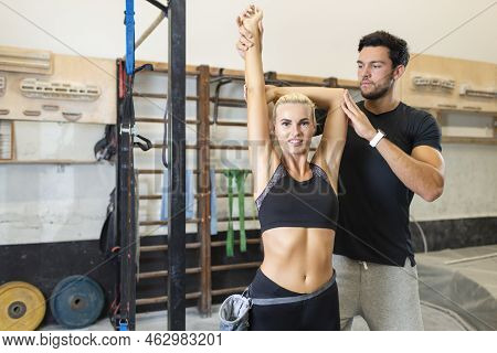 Caucasian Handsome Personal Trainer Instructor While Helping Young Blond Female Doing Correct Stretc