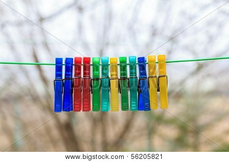 Row Of Colorful Clothespins Hanging On A Green Rope In A Gerden With Blurred Background