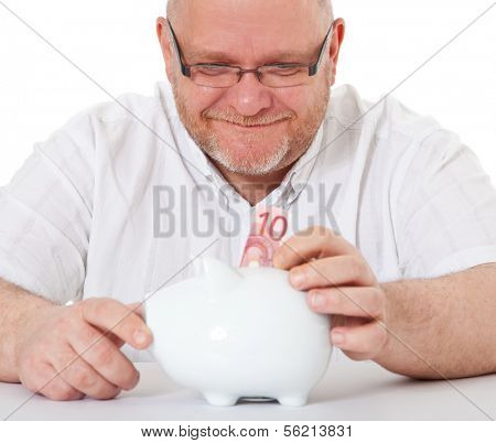 Charismatic middle aged man puts 10 euro into piggy bank. All on white background.