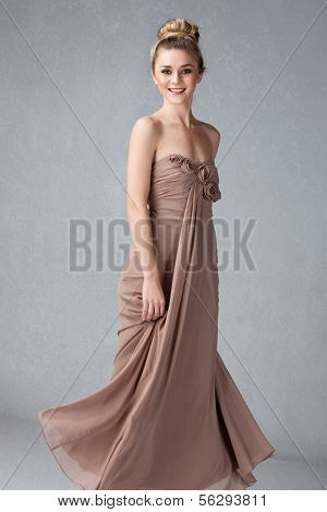 Young woman in long dress and hair in top knot bun on grey grunge studio background
