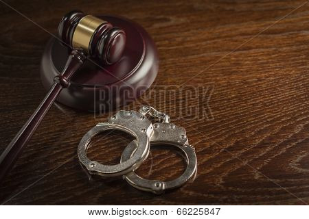 Gavel and Pair of Handcuffs on Wooden Table.
