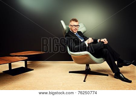 Imposing mature man in elegant suit sitting on a leather chair in a modern luxurious interior. Fashion. Business.
