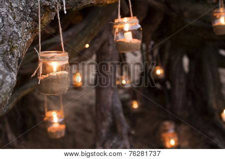 Beautiful decorated romantic place for a date with jars full of candles hunging on tree and standing