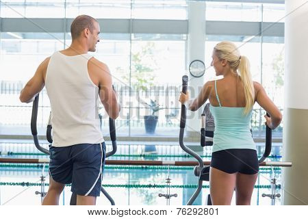Rear view of a fit young couple working on x-trainers at the gym