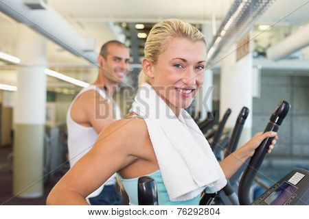 Side view portrait of a fit young couple working on x-trainers at the gym