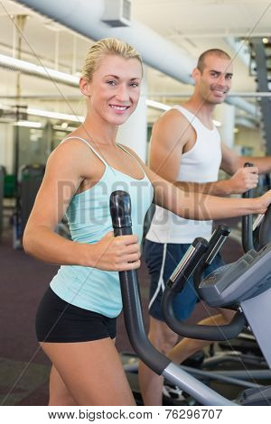 Side view of a fit young couple working on x-trainers at the gym
