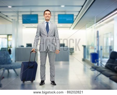 business trip, traveling, luggage and people concept - happy businessman in suit with travel bag over airport background