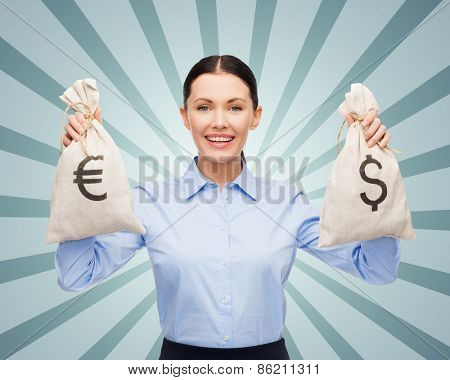 business, people, banking and finances concept - happy young businesswoman holding money bags with dollar and euro cash money over blue burst rays background