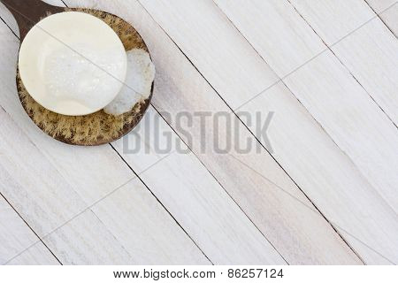 High angle shot of a sudsy bar of soap on a scrub brush. On a rustic wood surface the brush and soap are in the upper left corner of the frame leaving room for your copy.