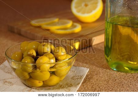 Green olives in a glass bowl, sliced lemon and a bottle of oil. Still life