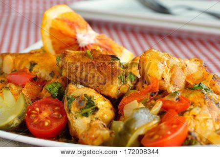 Braised chicken wings with orange , pickled cucumber and tomatoes. Close-up