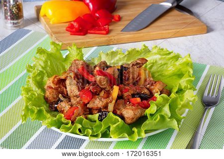Meat stew with prunes  and red sweet peppers .On green lettuce leaves. Against the background of a cutting board.