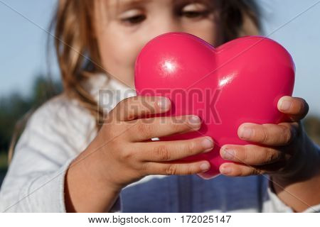 Little Girl Playing With A Red Plastic Heart. She Holds It In Her Hands