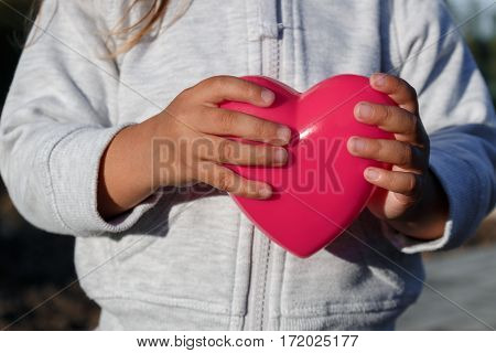 Little Girl Playing With A Red Plastic Heart. She Holds It In Her Hands