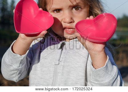 Little Girl Playing With A Red Plastic Heart. She Holds It In Her Hands