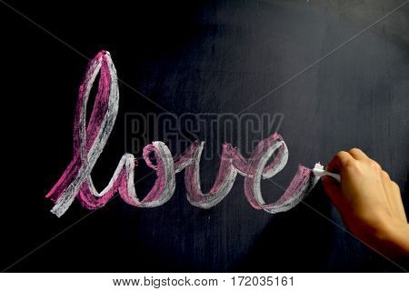 Image of a hand writing love word by chalk on blackboard.