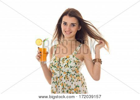 happy young brunette woman in sarafan with floral pattern drinks orange cocktail and smiling on camera isolated on white