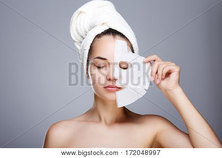 Girl with half rended white mask. Model pulling away mask from her face. Closed eyes. Head and shoulders, studio, indoors