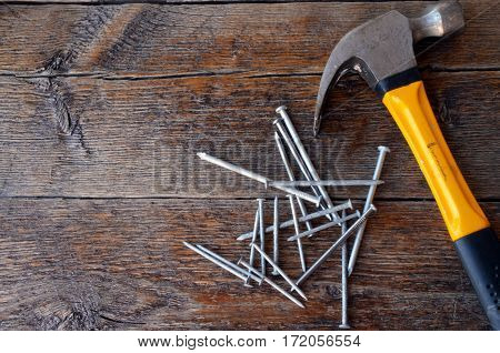 A top view image of an old used yellow hammer and a pile of nails on a wooden workbench.