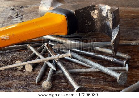 A low angle image of an old used yellow hammer and a pile of nails on a wooden workbench.