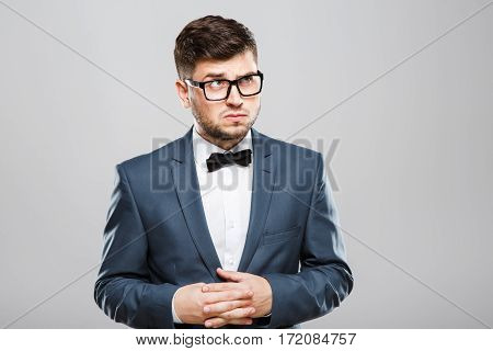 Stylish young man in suit with bow and eyeglasses. Fingers crossed, looking up with suspicion. Jacket, bow, official outlook. Waist up, studio, indoors