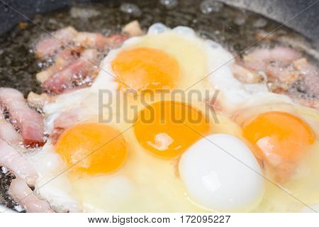 Frying eggs with sliced bacon in the hot oil.