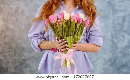 Two hands with bouquet of tulips on the blue wall background