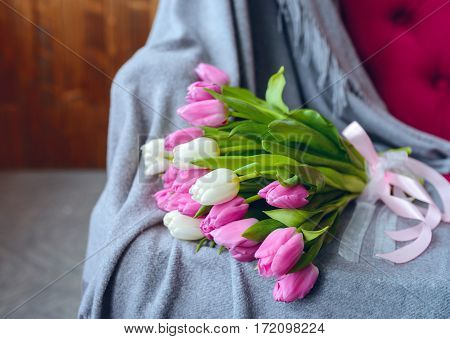 Bouquet of pink and white tulips with pink ribbon on gray blanket at pink sofa