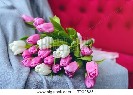 Bouquet of pink and white tulips with pink ribbon on gray blanket at pink sofa