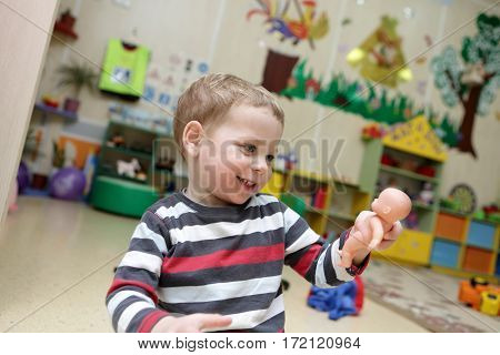 Сhild holding and looking at doll in kindergarten