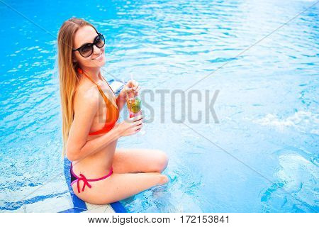 Young Pretty Blond Woman In A Orange Bikini And Sunglasses Enjoying Cocktail In A Swimming Pool