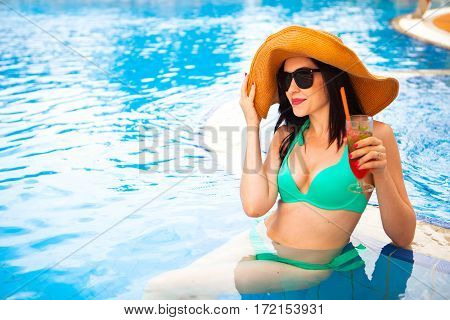 Beautiful Brunette Woman Wearing A Hat And Sunglasses, Enjoying Cocktail In A Swimming Pool, Summer