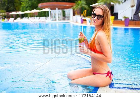 Young Pretty Blond Woman In A Orange Bikini And Sunglasses Enjoying Cocktail In A Swimming Pool