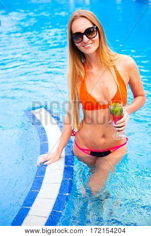 Young Pretty Blond Woman In A Orange Bikini And Sunglasses Enjoying Cocktail In A Swimming Pool