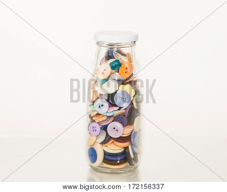 a glass bottle of plastic buttons of various colors
