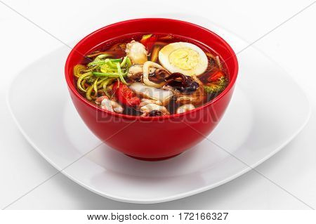 Ramen soup seafood, peppers, zucchini, udon noodles, egg, leeks in a white plate on a white background