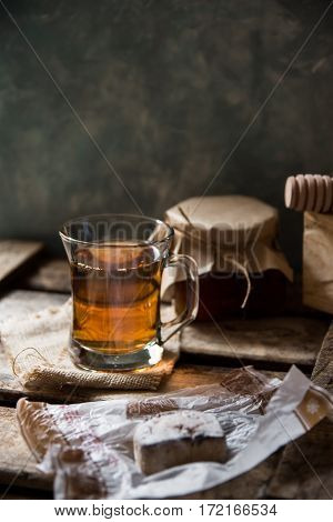 Glass cup with hot tea with jar of honey or jam wood spoon Spanish cookie polvoron on vintage box grey wall backgroundrustic vintage interiorcozy atmosphere