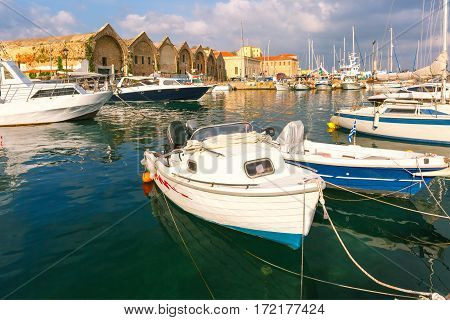 Chania Arsenals, the Venetian shipyards, and fishing boats in old harbour of Chania with Lighthouse in cloudy summer morning, Crete, Greece
